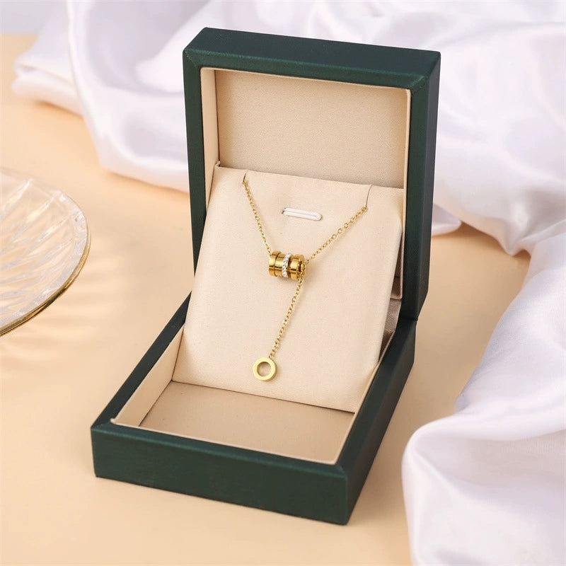 Gold-tone cylinder and ring pendant necklace in green gift box with ring charms
