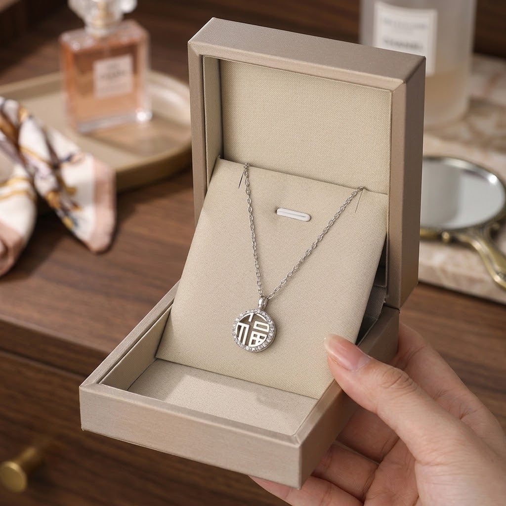 Silver round charm necklace with monogram pendant, hanging from chain in box.