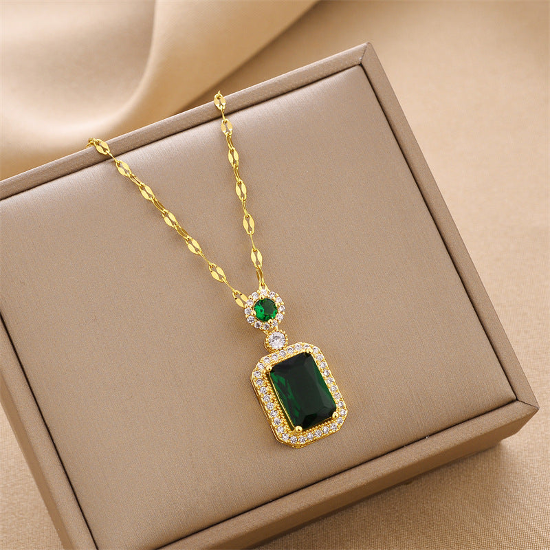 Gold charm necklace with a large square green gemstone pendant and emerald accents