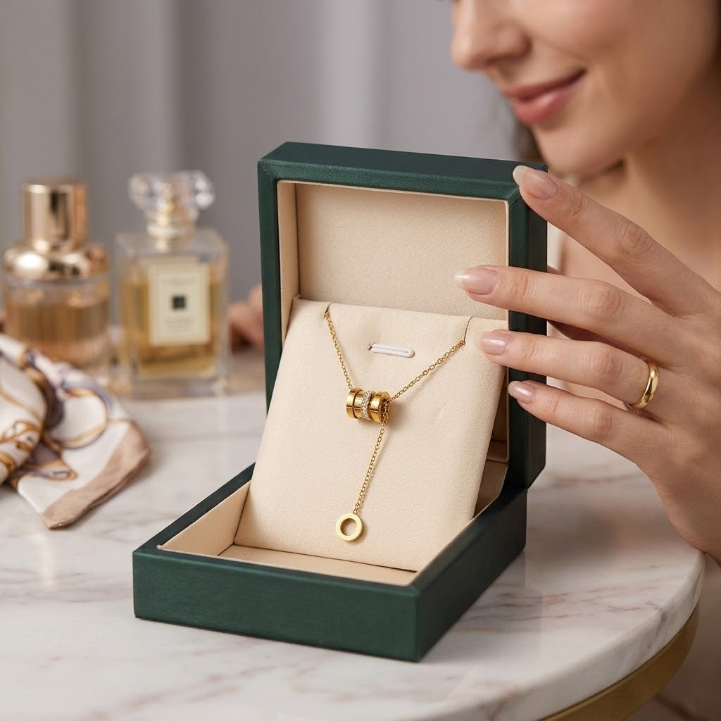 Gold-tone cylinder and ring pendant necklace in green gift box, held up for viewing