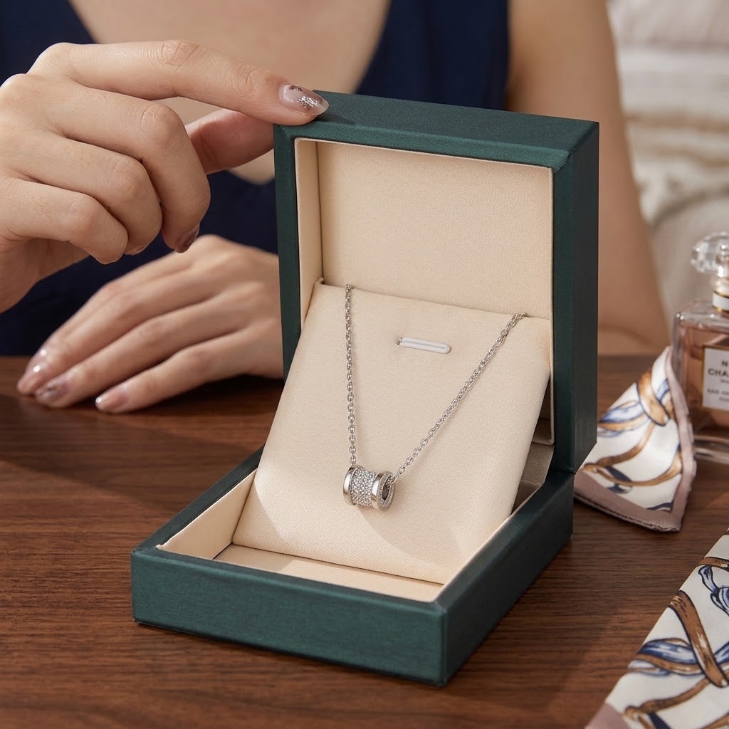 Silver cylindrical pendant necklace displayed in green gift box with cylinder charm on chain.