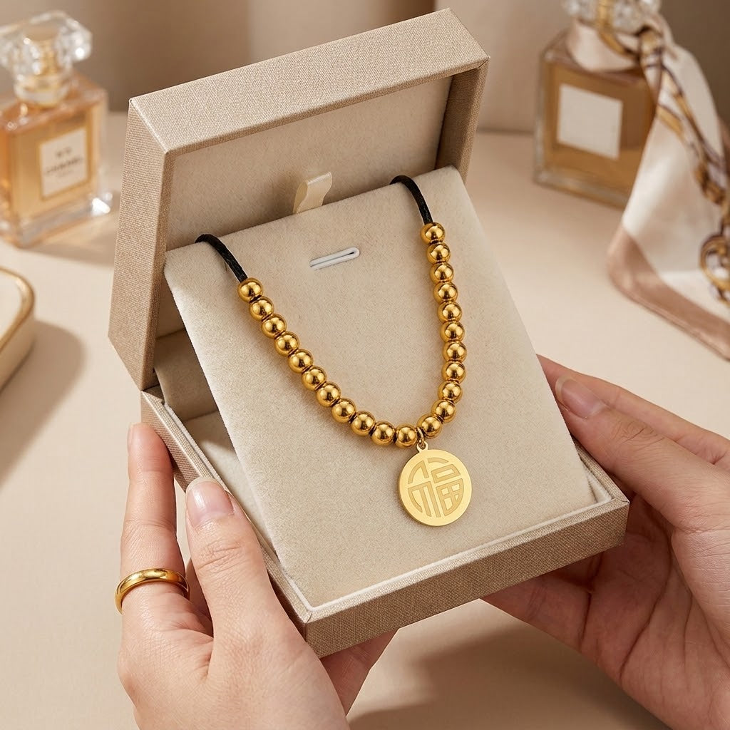 Gold beaded pendant necklace with black cord and round disc charm, shown in gift box