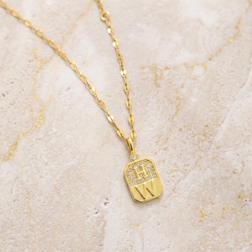 Gold-tone necklace with square crystal tag charm and chain, dangling W initial
