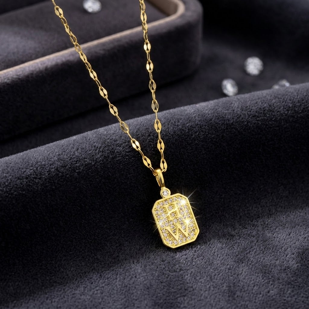 Gold-tone necklace with square rhinestone tag charm and W initial, on black display
