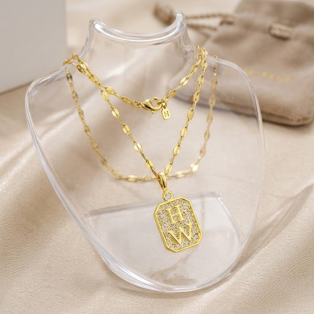Layered gold-tone necklace with square W initial crystal tag charm on clear stand