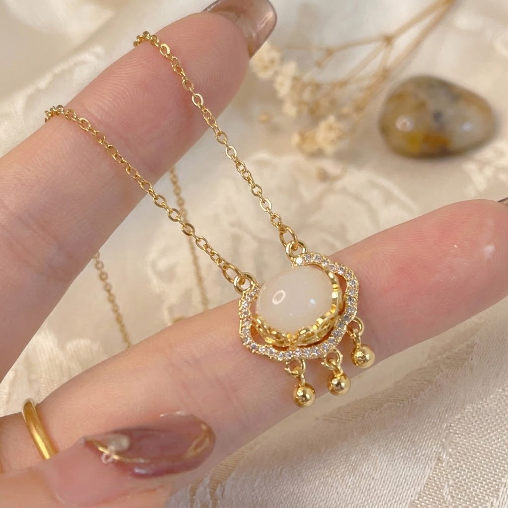 Gold-tone halo charm pendant necklace with oval white stone and dangling bead charms