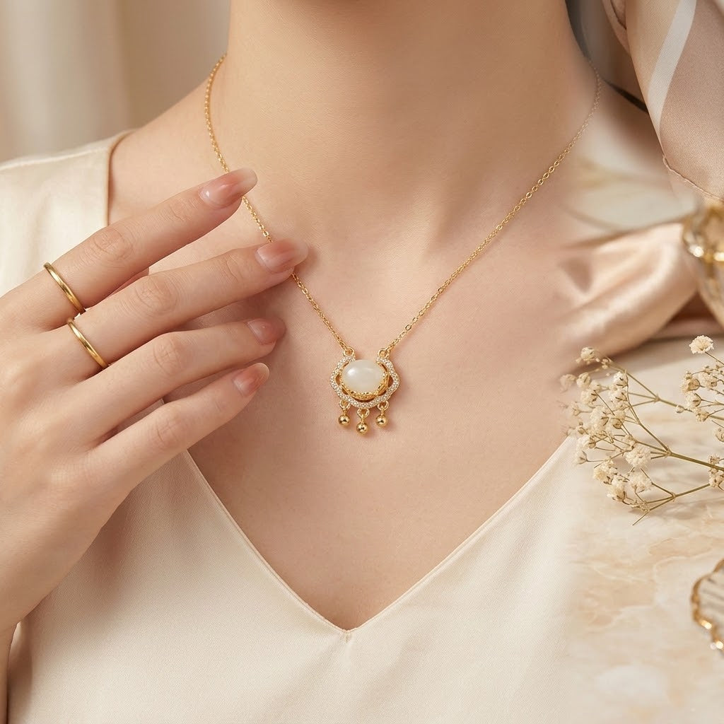 Gold-tone oval halo charm necklace with white stone center and dangling bead fringe