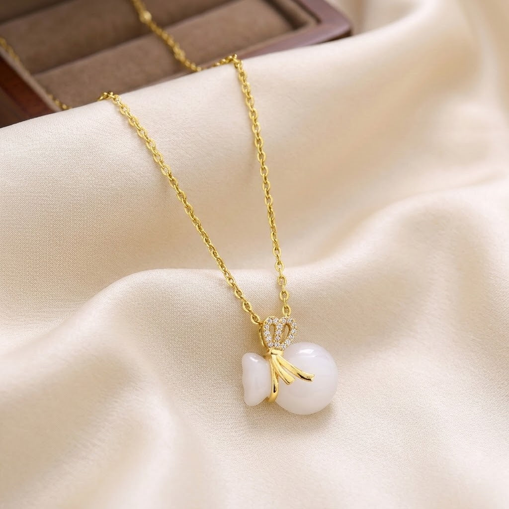 Gold-tone necklace with crown charm and white bead pendant with bow details