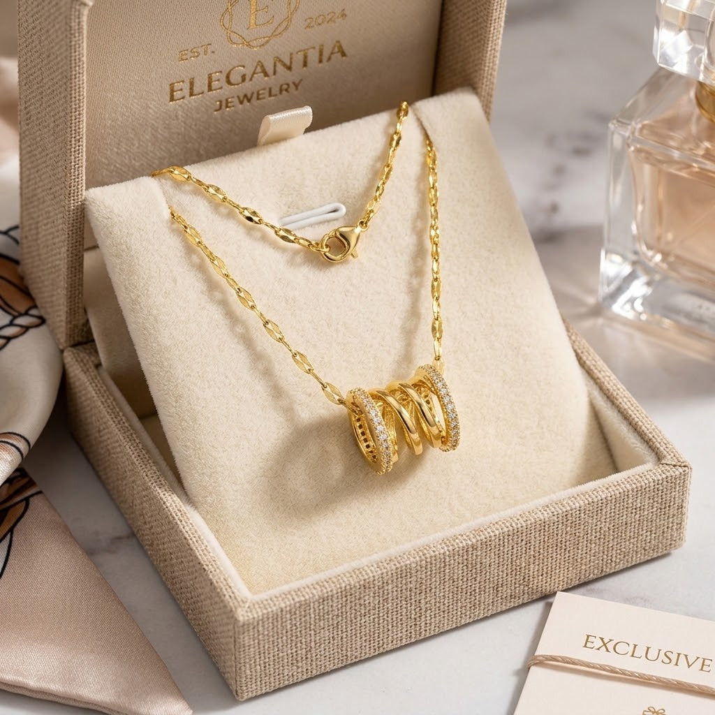 Gold-tone coil pendant necklace with three-ring charm and clasp, shown in gift box