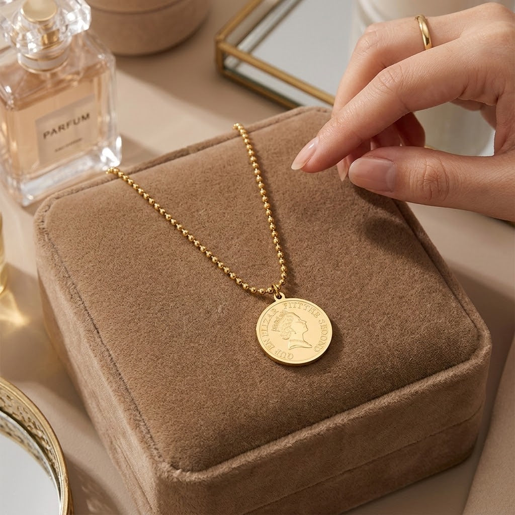 Gold coin pendant necklace with beaded chain, round medallion held over jewelry box