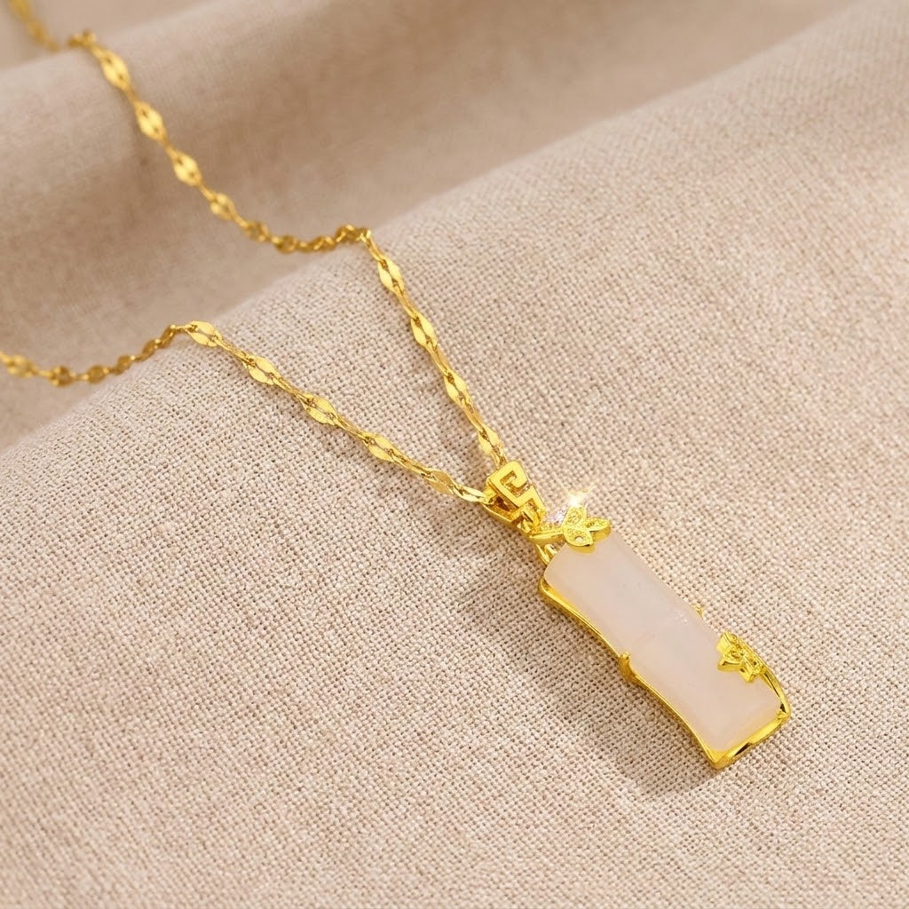 Gold necklace with pale pink segmented pendant and small heart-patterned charms