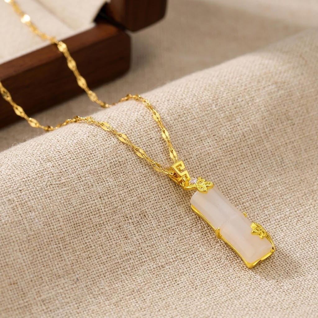 Gold necklace with pale pink segmented pendant and filigree heart motif on chain