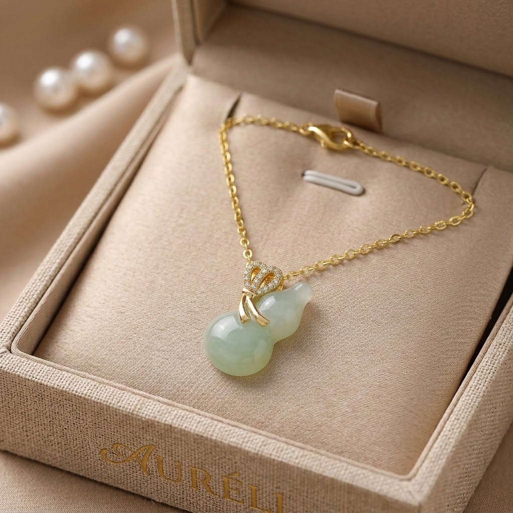 Gold-tone necklace with crown charm and light aqua bead pendant on beige jewelry box