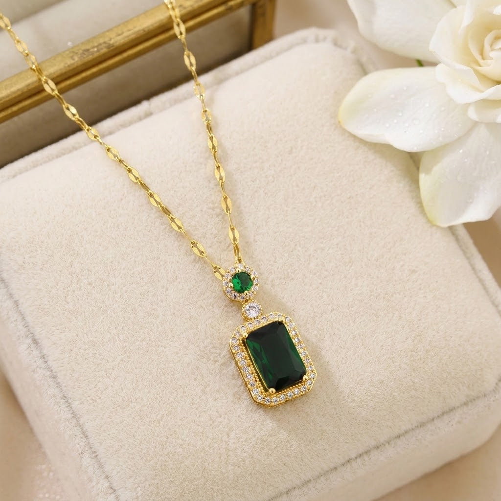 Gold-tone gemstone charm necklace with green square pendant, shown on a display cushion