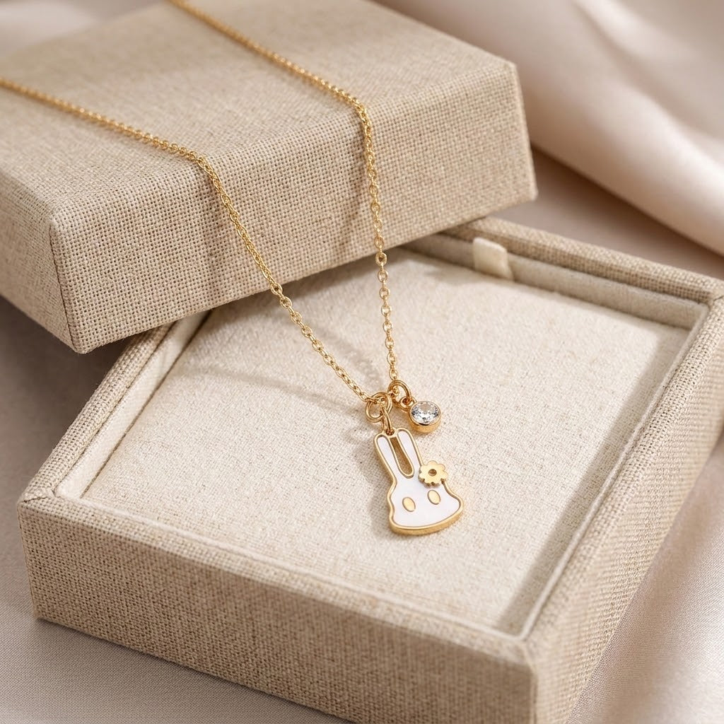 Gold-tone bunny pendant necklace with flower accent on beige jewelry box