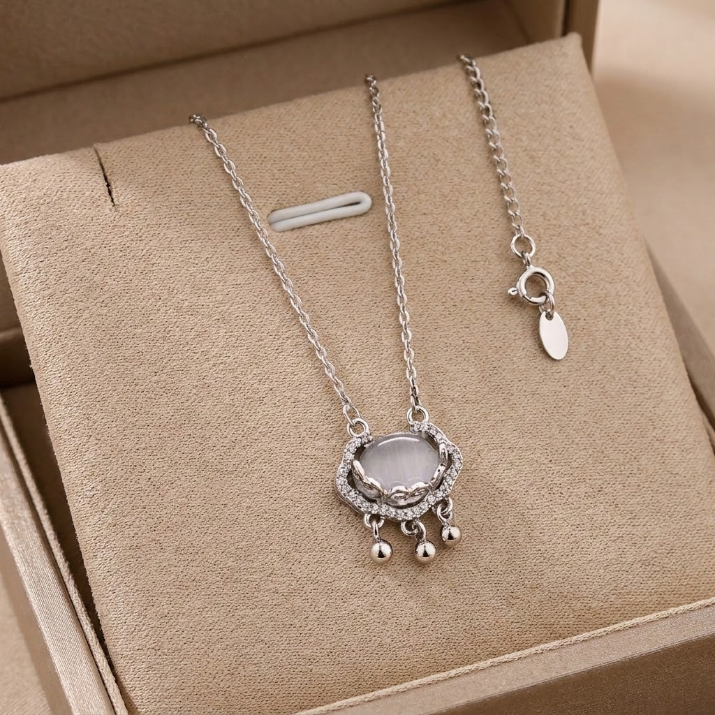 Silver-tone halo charm necklace with oval stone and dangling bead accents on tray
