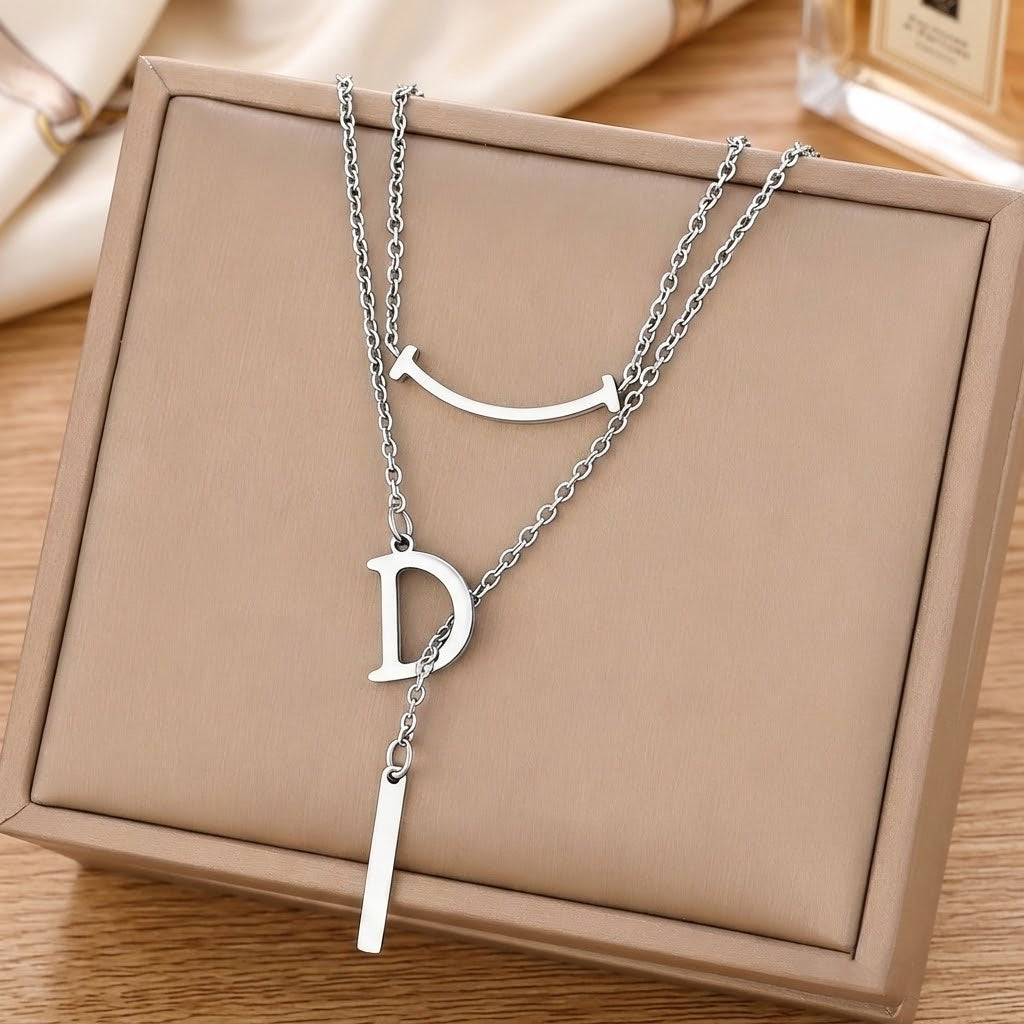 Silver letter D charm necklace laid in a gift box with curved smile charm