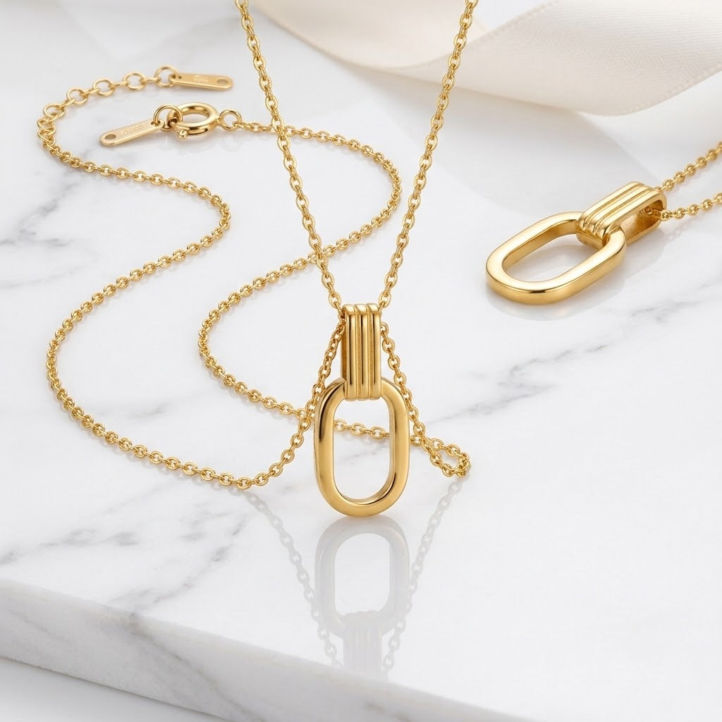 Gold O-shaped charm necklace set with chain and open oval pendant laid on marble
