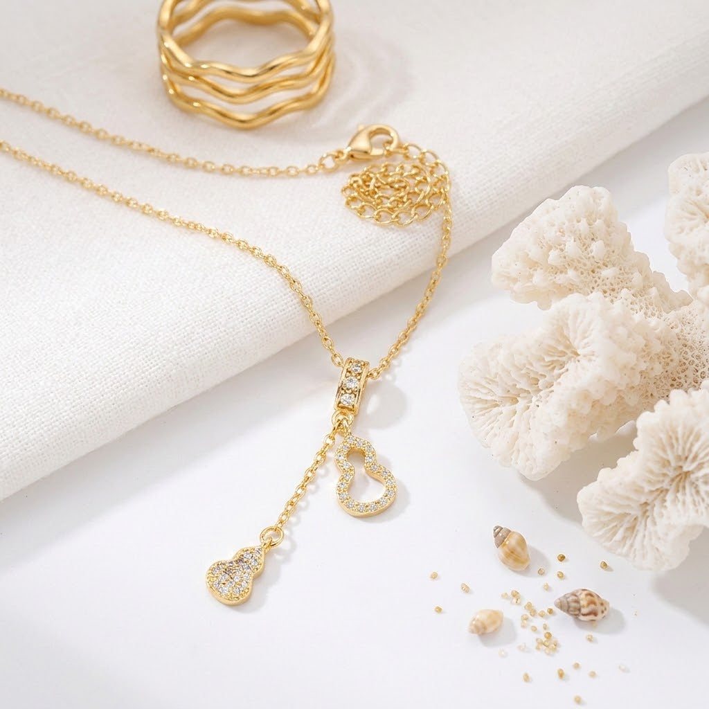 Gold-tone charm necklace with a fine chain and teardrop center pendant plus two hearts