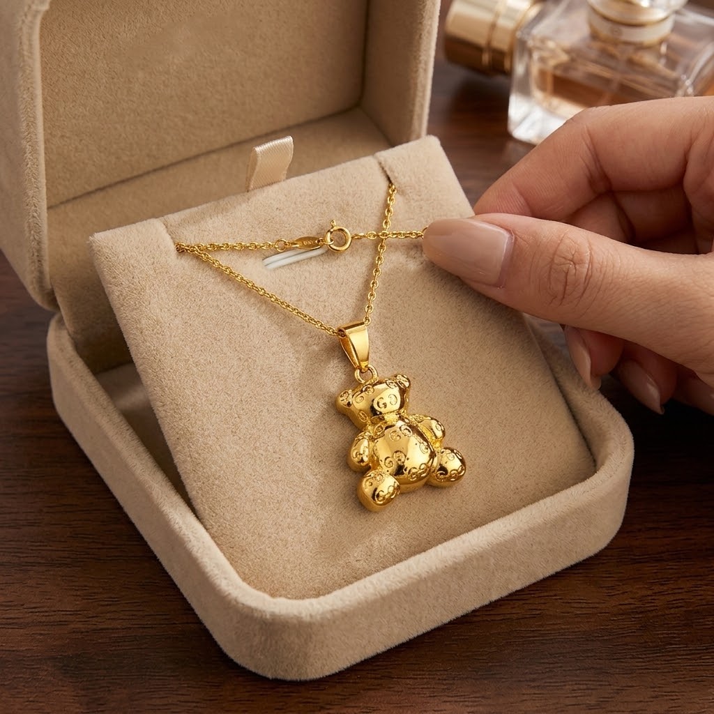 Gold bear pendant necklace held in hand above beige jewelry tray