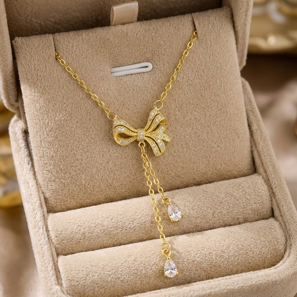 Gold bow charm necklace with crystal drops on chain, shown in a beige jewelry box