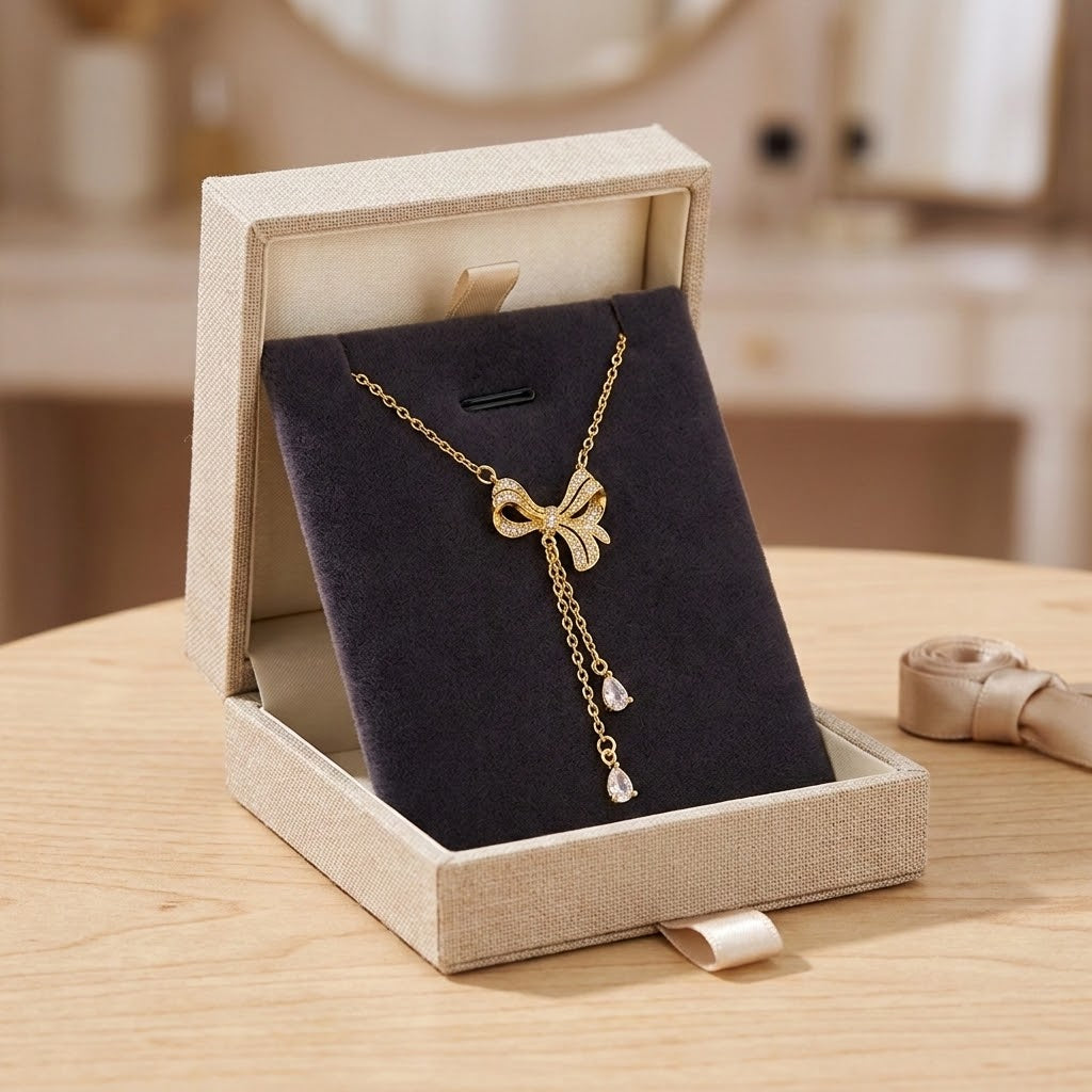 Gold bow charm necklace with crystal pendants on chain, on black jewelry display