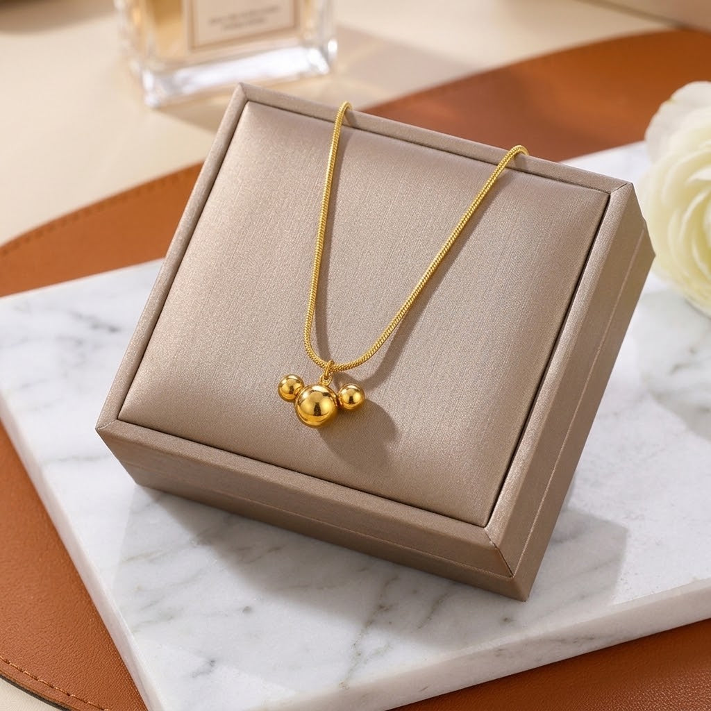 Gold triple ball charm necklace with linked chain, shown in beige display box