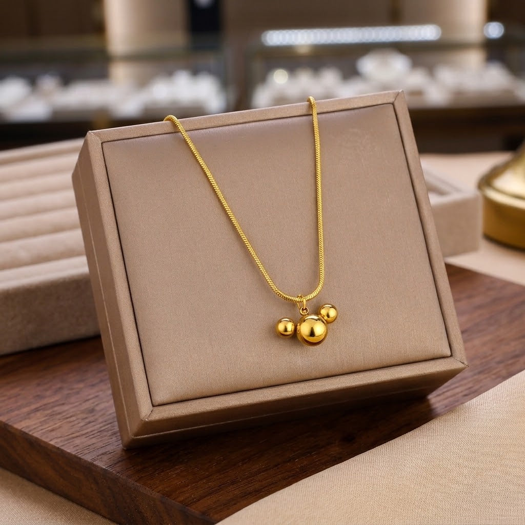 Gold-tone triple ball charm necklace with linked chain on wooden surface