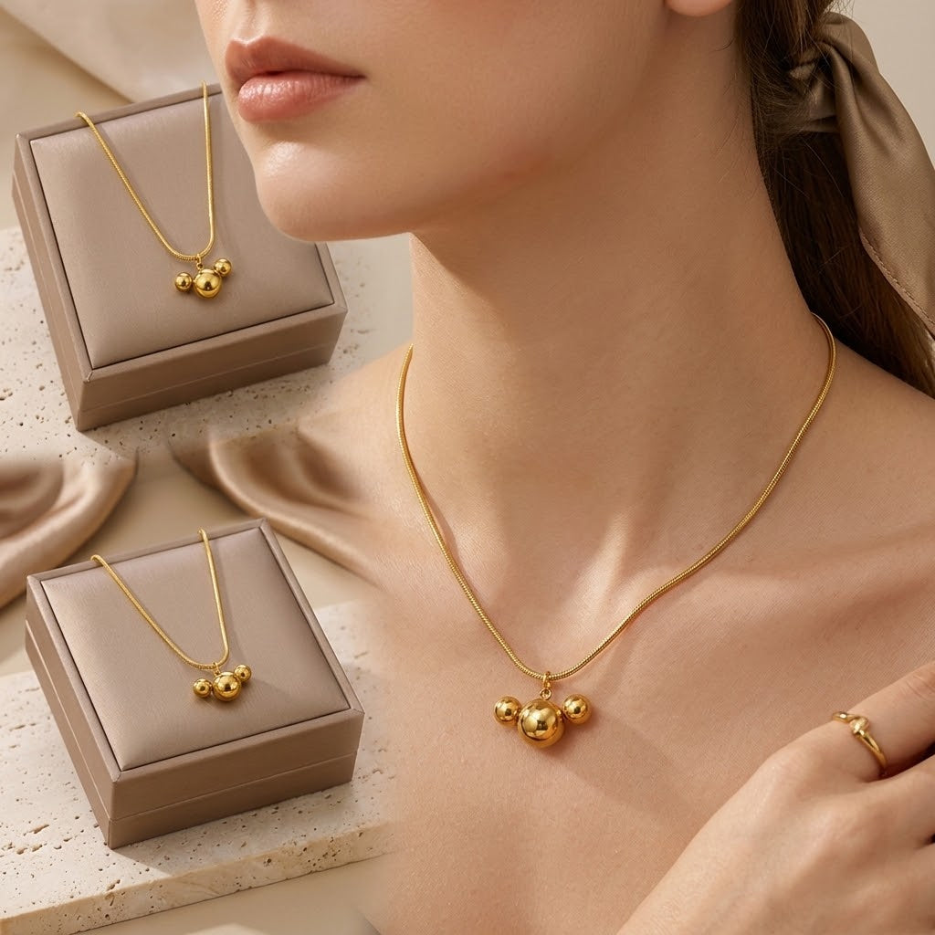 Gold-tone triple ball charm necklace close-up on neck with small display boxes